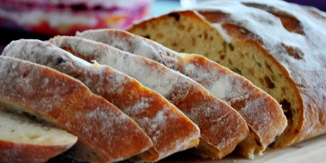 Pokrojony chleb z pomidorami, posypany mąką, leży na desce. W tle widać sałatkę.