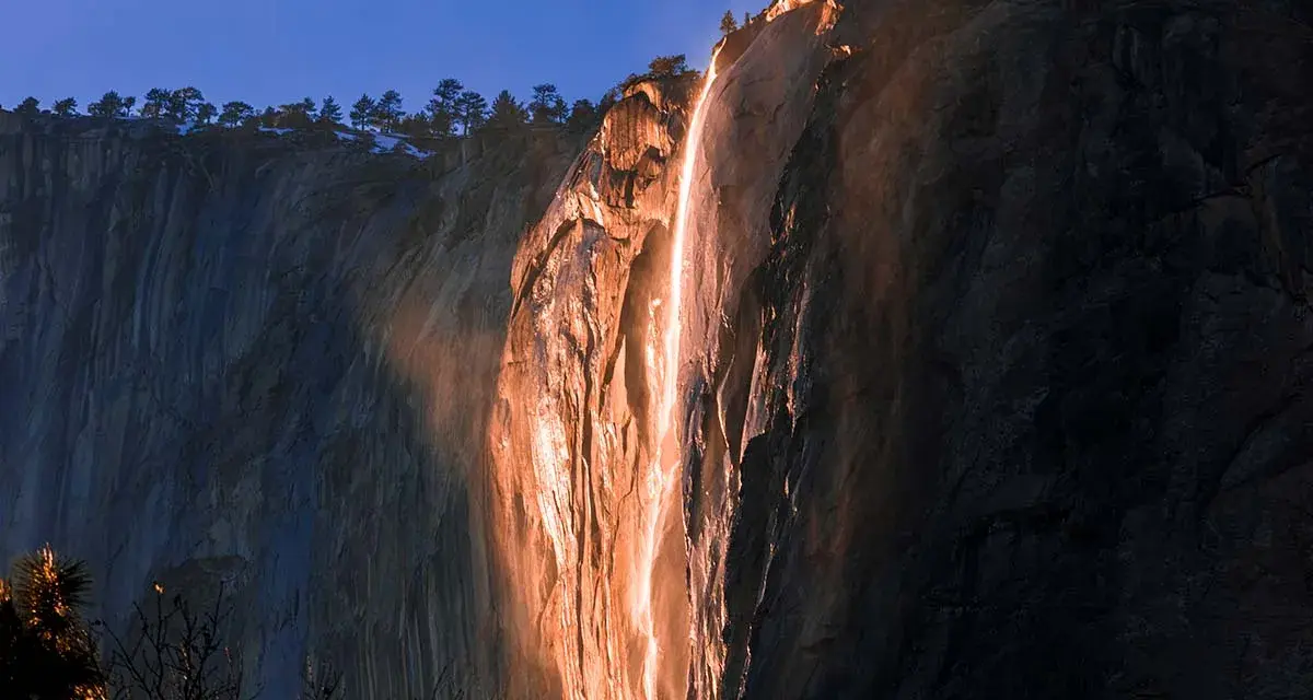 La luz del atardecer ilumina una cascada de fuego en un acantilado rocoso, creando un espectáculo natural.