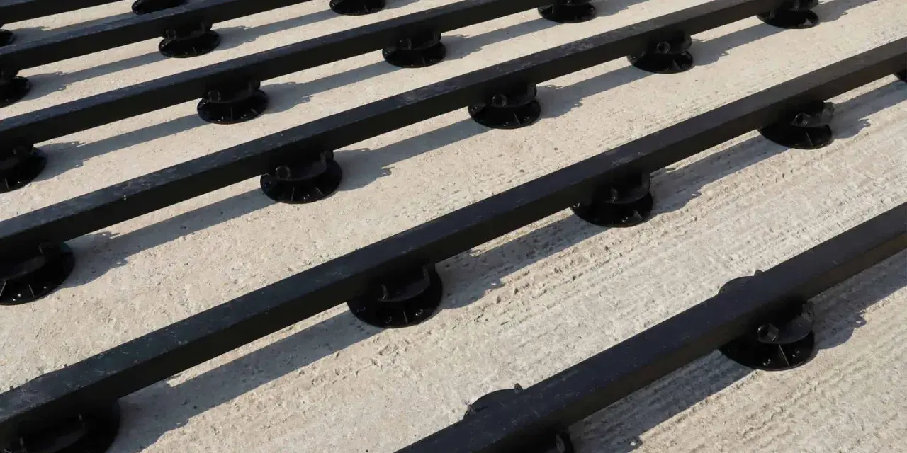 Rows of black synthetic lumber are elevated on black adjustable pedestals, creating a modern deck base on a concrete surface.