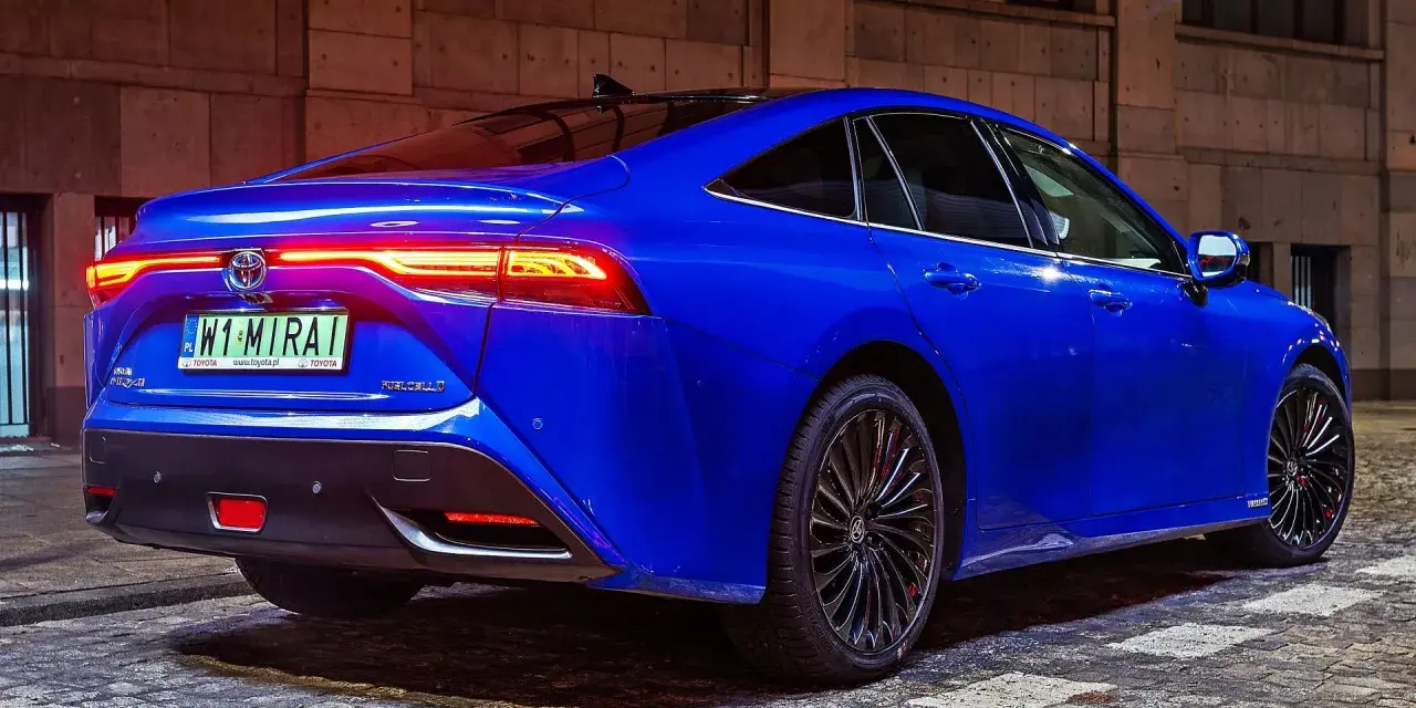 Niebieska Toyota Mirai z podświetlonymi światłami tylnymi stoi na brukowanej ulicy nocą.