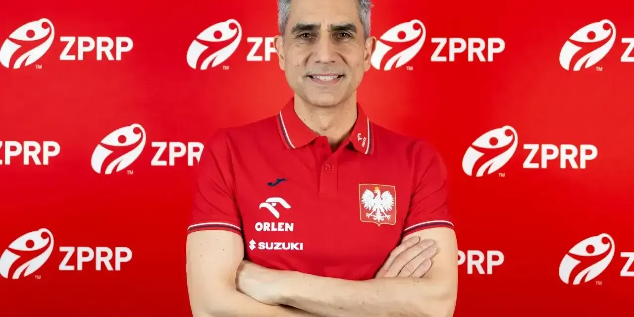 Uśmiechnięty mężczyzna, były trener piłkarzy ręcznych, w czerwonej koszulce z godłem Polski i logo ZPRP.