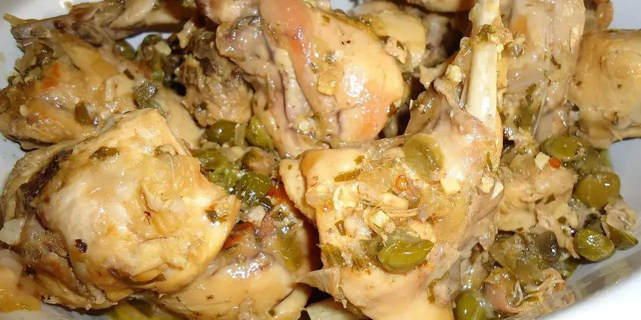 Piatto fumante di coniglio alla cacciatora in bianco, con olive verdi e erbe aromatiche. Un classico della cucina italiana.
