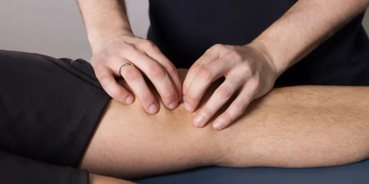 Fizjoterapeuta wykonuje masaż kolana, co jest częścią leczenia chondropatii rzepki.