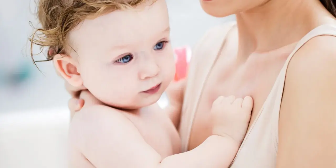 Ein Baby mit blauen Augen und zerzaustem Haar wird von seiner Mutter gehalten. Es ist fast 46 Wochen alt und durchläuft einen Entwicklungsschub.