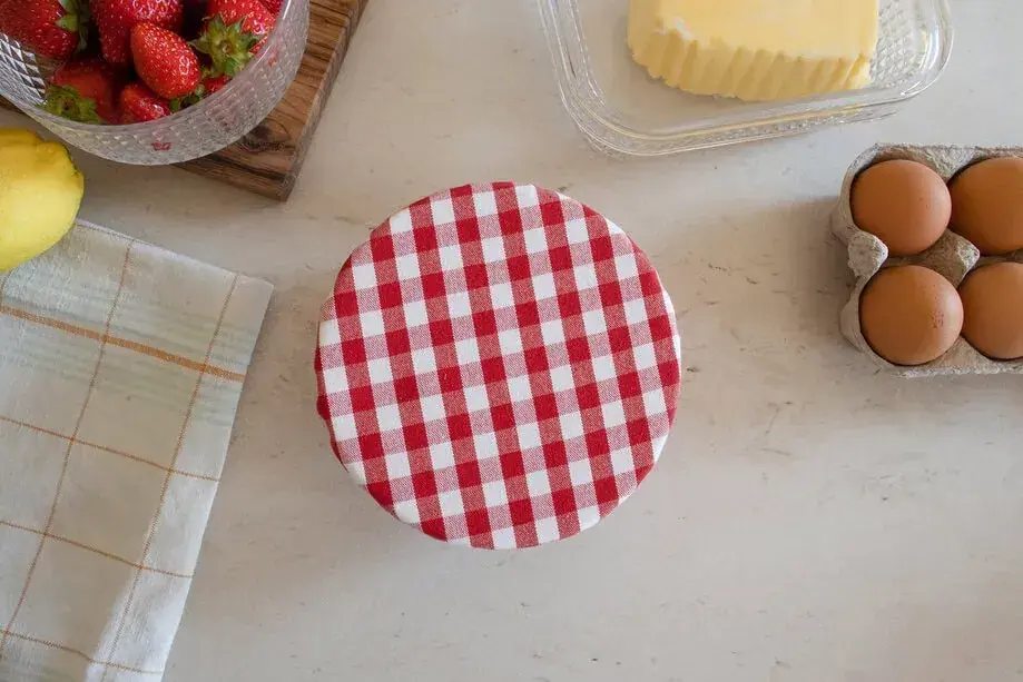 Préparation d'une charlotte alimentaire : fraises, citron, beurre, œufs et un couvercle à carreaux rouges et blancs.