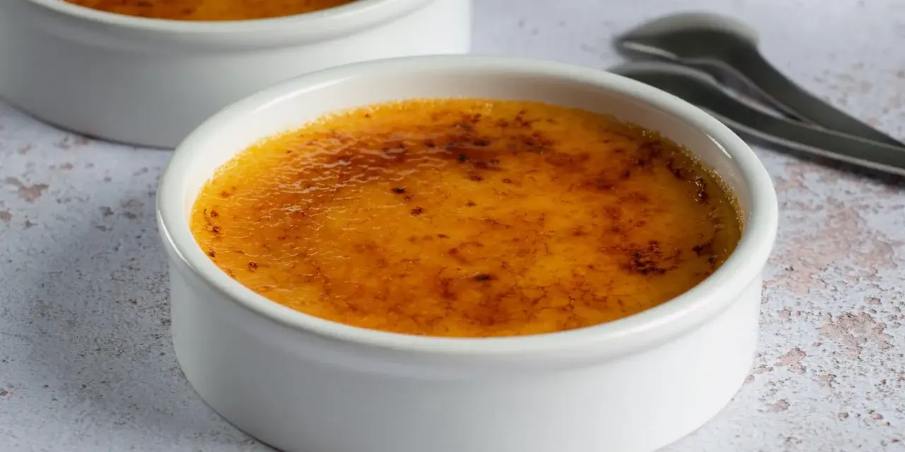 Dwa kremowe desery w białych naczyniach, z chrupiącą, karmelizowaną skórką. Crème brûlée czy crema catalana? Wybór należy do Ciebie!