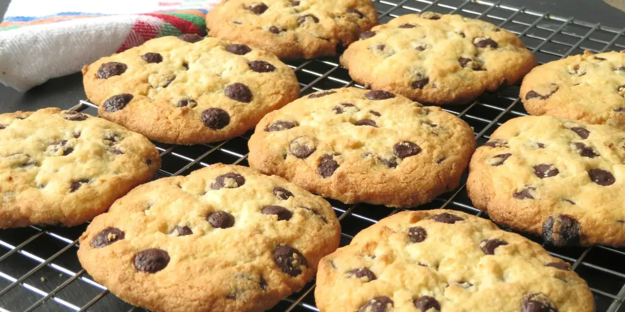 Un montón de galletas con pepitas de chocolate recién horneadas, doradas y deliciosas, enfriándose en una rejilla.
