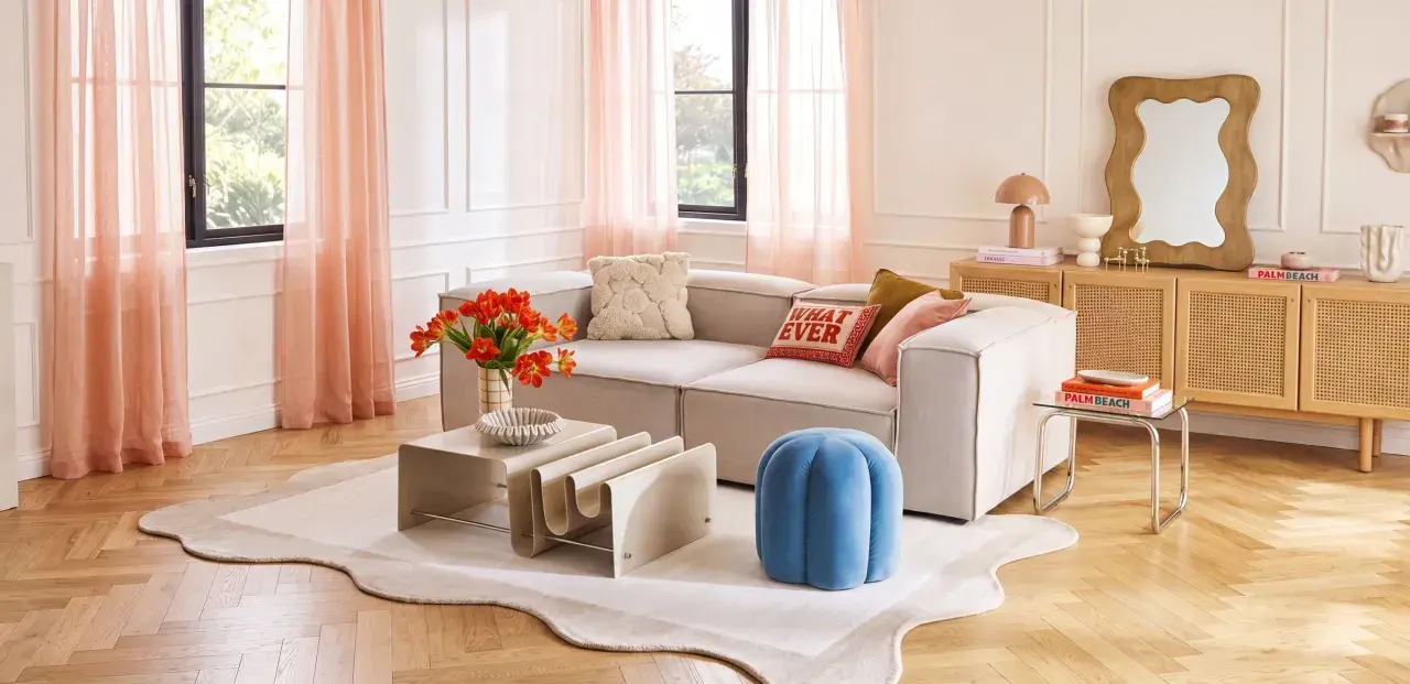 Ein Wohnzimmer mit beigem Sofa, orangefarbenen Tulpen und Korbmöbeln. Die sanften Pfirsichtöne der Vorhänge und Kissen zeigen, welche Farben passen zusammen.
