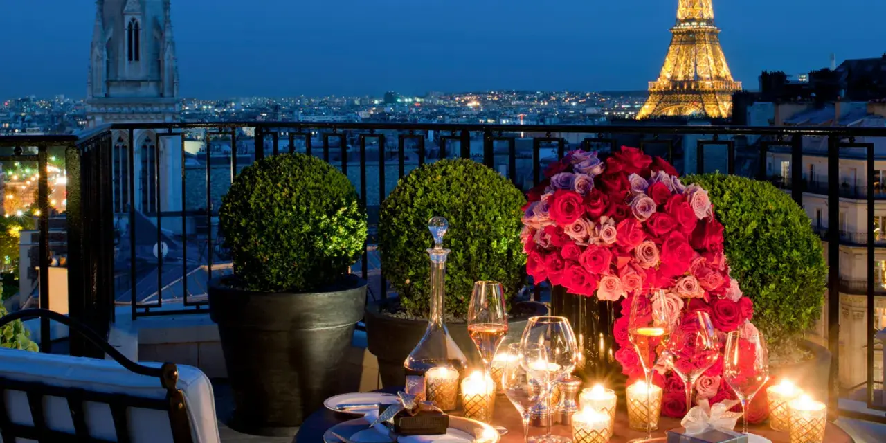 Cena romántica en París para San Valentín. Mesa con rosas, velas y Torre Eiffel iluminada al fondo.