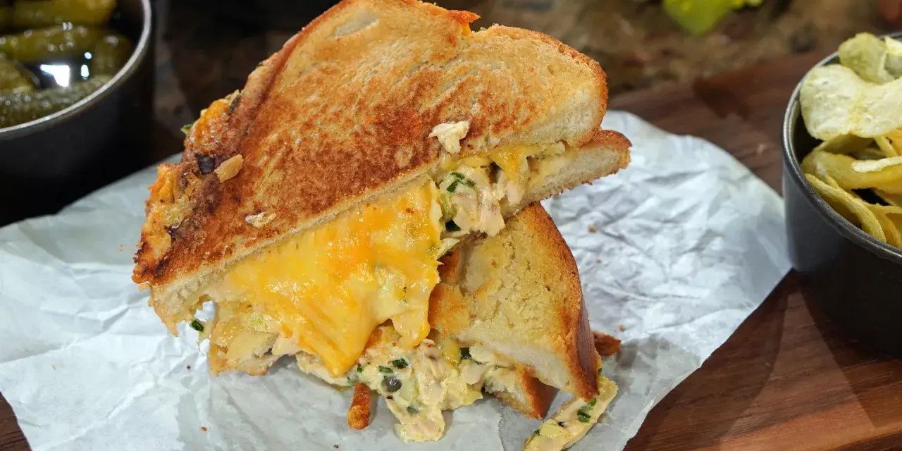 Ein köstlicher Tuna Melt mit geschmolzenem Käse, serviert mit Gurken und Chips.
