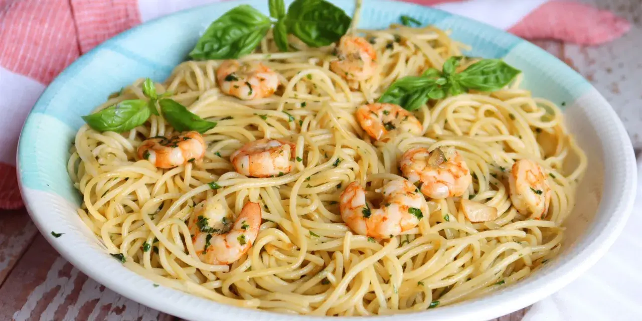 Un plato de espaguetis con gambas, adornado con hojas de albahaca fresca y perejil picado.