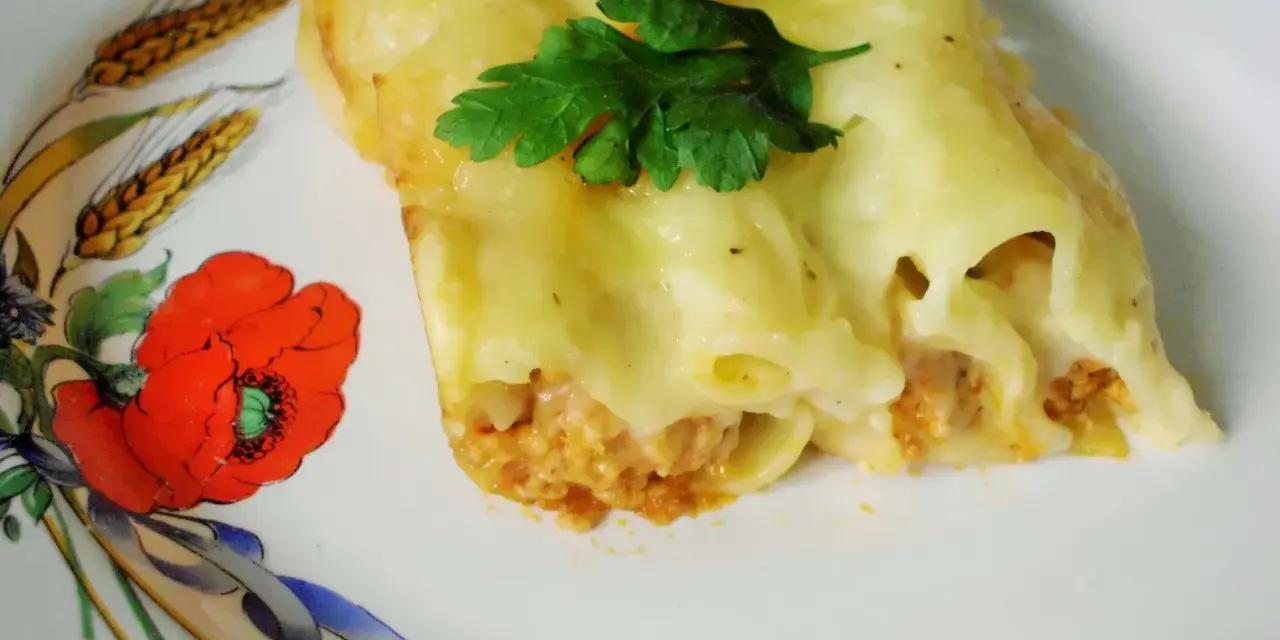 Cannelloni z mięsem i beszamelem przepis. Pyszne danie zapieczone pod beszamelem, udekorowane natką pietruszki, na talerzu z makami.