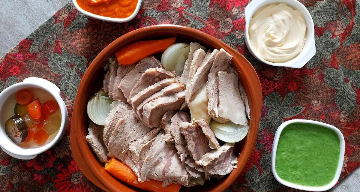 Un invitante bollito di carne, affettato e servito con carote, cipolle e tre salse: una rossa, una bianca e una verde.
