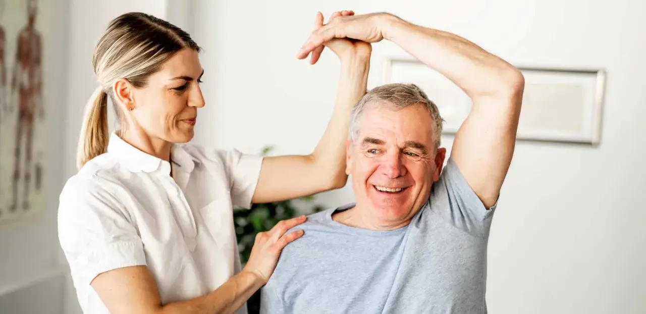 Physiotherapeutin unterstützt Mann bei Übungen zur Wiederherstellung der Beweglichkeit nach Schlaganfall. Verordnung Physiotherapie nach Schlaganfall wird umgesetzt.