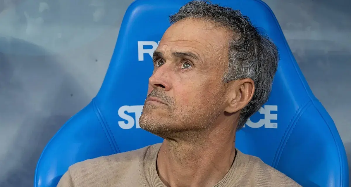 Luis Enrique, kto jest trenerem PSG, siedzi na niebieskiej ławce, zamyślony.