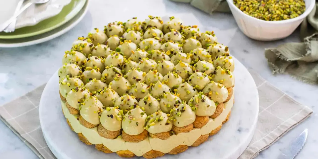 Torta rotonda con tante piccole meringhe verdi e granella di pistacchio, un delizioso tiramisù al pistacchio.
