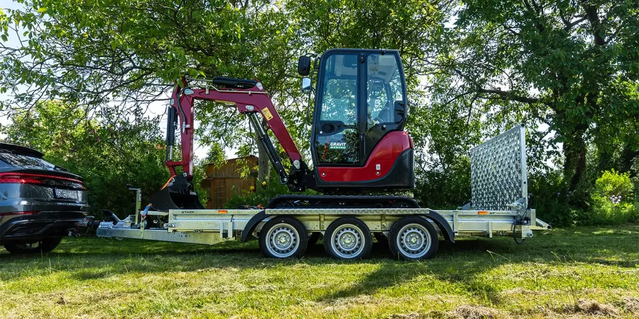 Czerwony minikoparka na przyczepie, gotowa do transportu. Posiadanie odpowiedniego **kod 96 prawo jazdy** jest kluczowe do przewożenia takich maszyn.