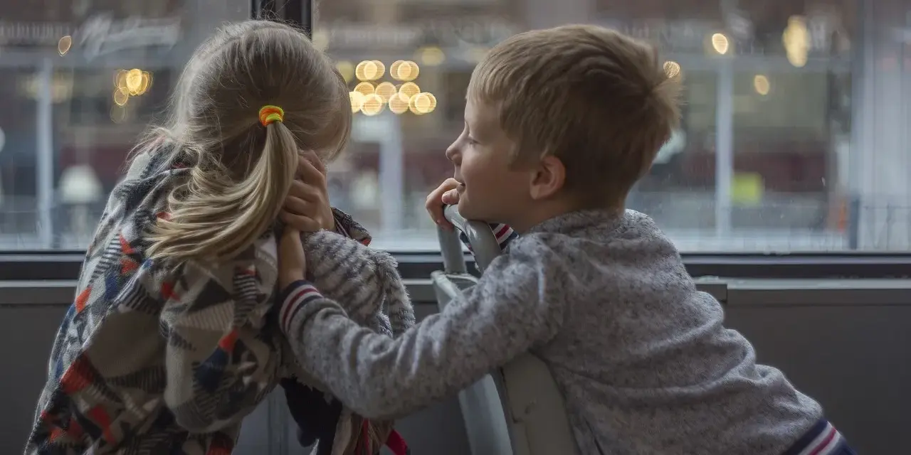 Bambina con disturbo della comunicazione sociale si nasconde, mentre un bambino le parla con un sorriso.