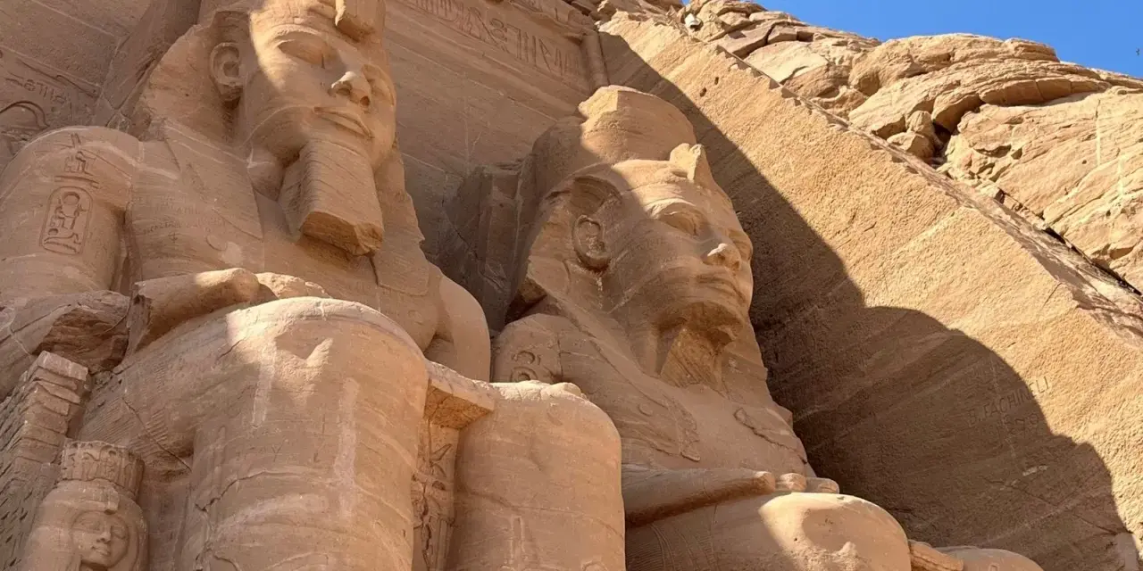 Gigantyczne kamienne posągi faraonów w Abu Simbel, Egipt, na tle skalnej ściany i błękitnego nieba.