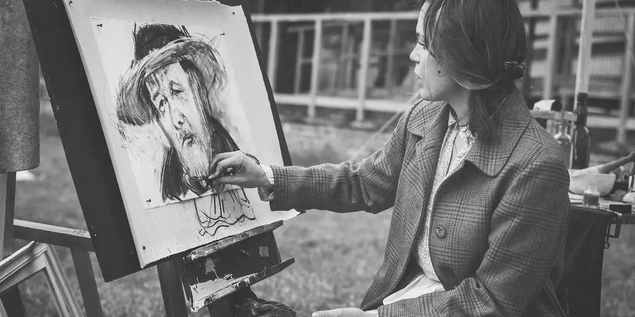 Artystka tworzy portret węglem. Jej ręka z pędzlem zbliża się do płótna, gdzie widoczna jest plama rysunek.