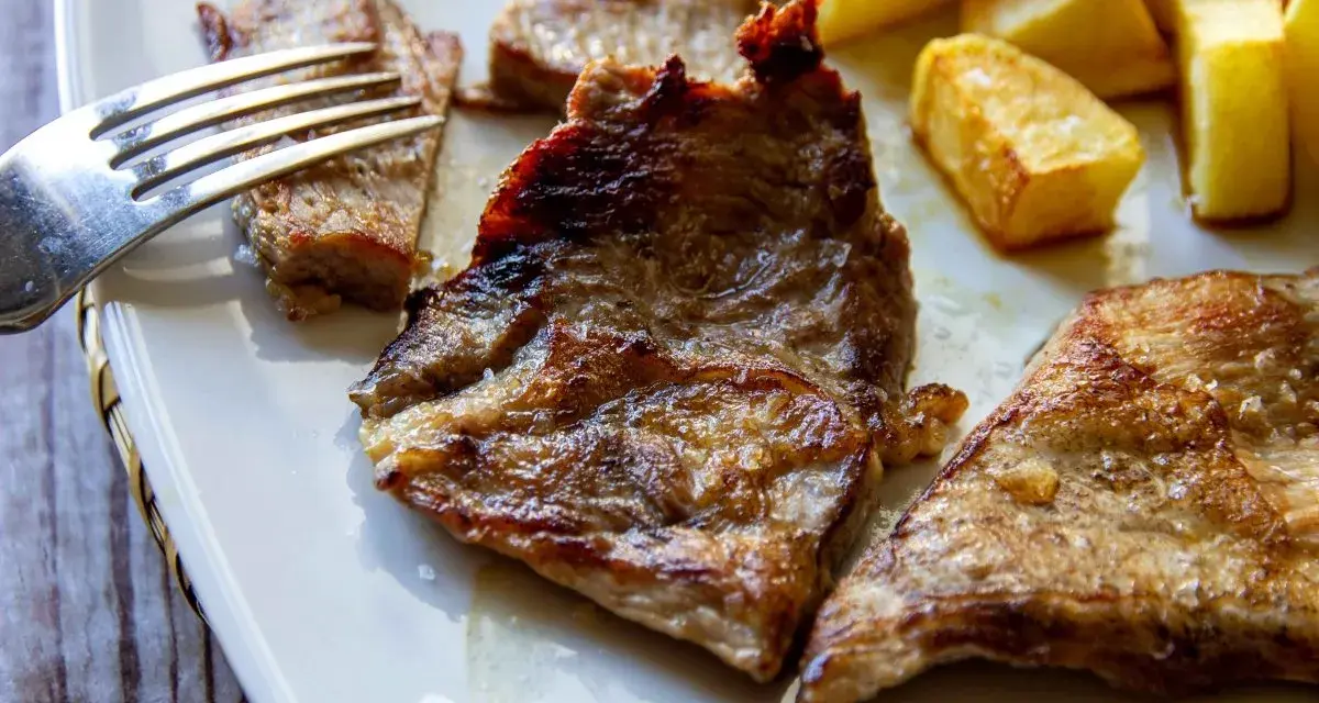 Jugosa blanqueta de cerdo a la plancha, servida con patatas fritas doradas. Un plato perfecto para disfrutar.