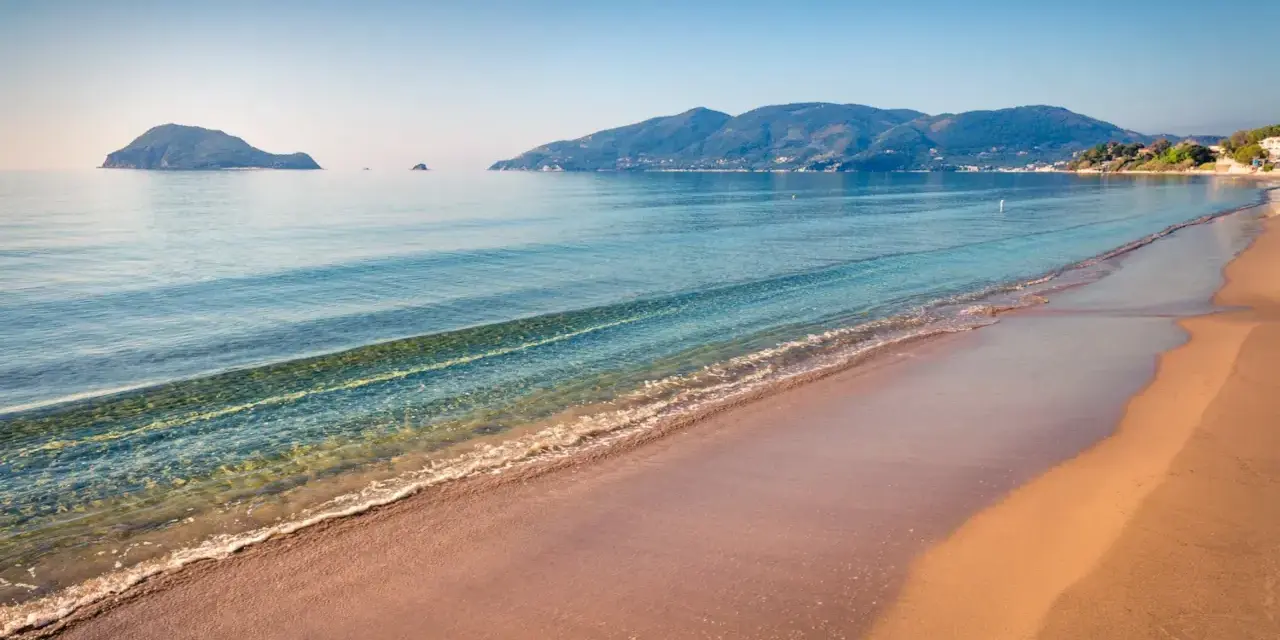 Spokojna plaża Caretta z łagodnymi falami i wyspami w oddali. Idealne miejsce na relaks.