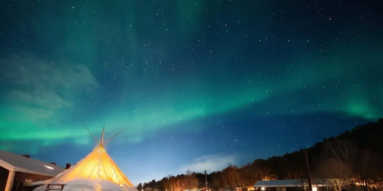Nocne niebo nad nordkapp camping rozświetla zorza polarna. W dole ośnieżony teren i oświetlony namiot.