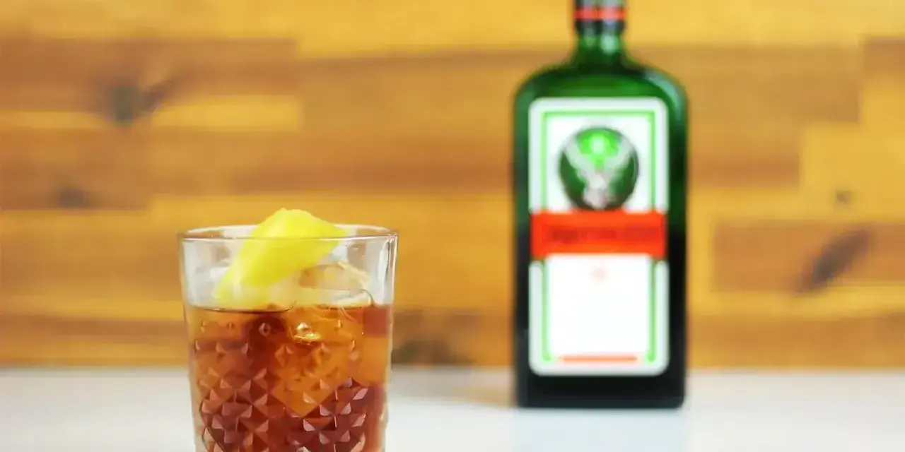 Jägermeister z pomarańczą to świetny drink. Na zdjęciu drink z lodem i plasterkiem pomarańczy obok butelki Jägermeister.