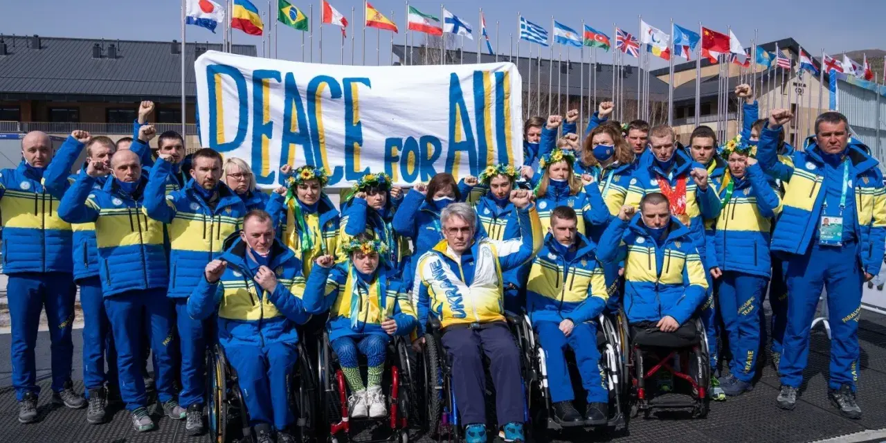 Ukraińska drużyna paraolimpijska z podniesionymi pięściami przed transparentem "Peace for All". Nadzieja na pokój na igrzyskach paraolimpijskich 2026.