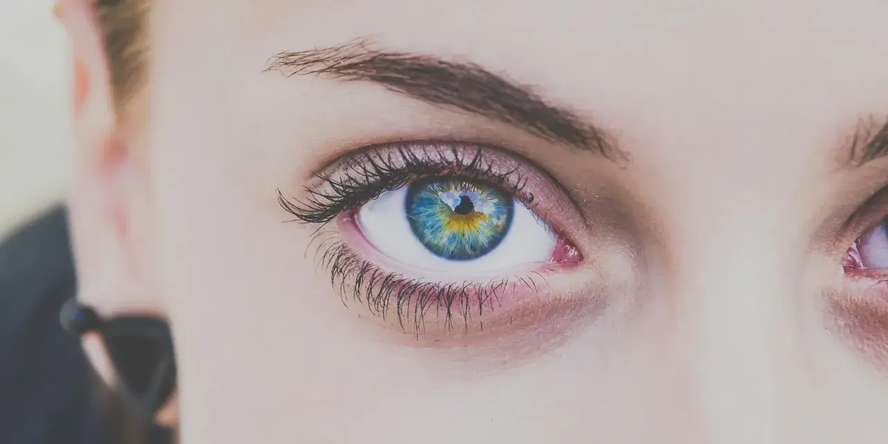 Ojo con iris azul y amarillo, pestañas largas y cejas definidas tras un laminado de cejas.