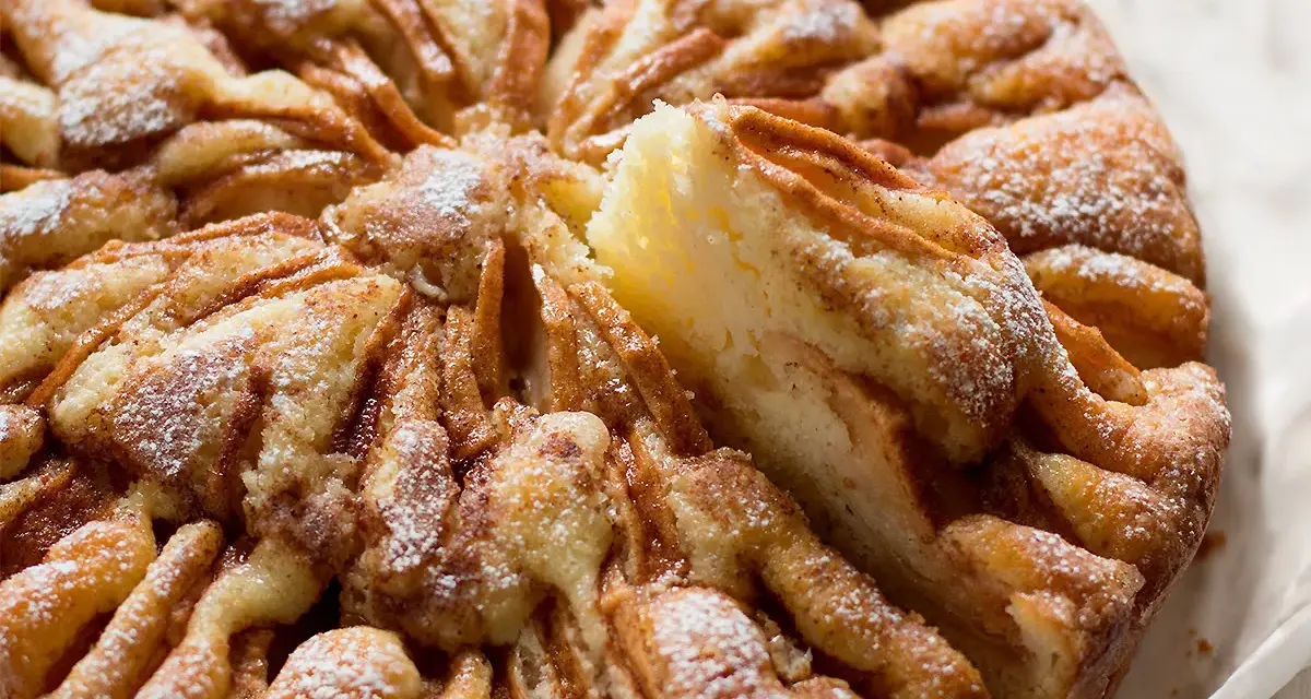 Una deliziosa torta di mele, cosparsa di zucchero a velo, con una fetta appena tolta che rivela la morbidezza dell'impasto e le mele caramellate.