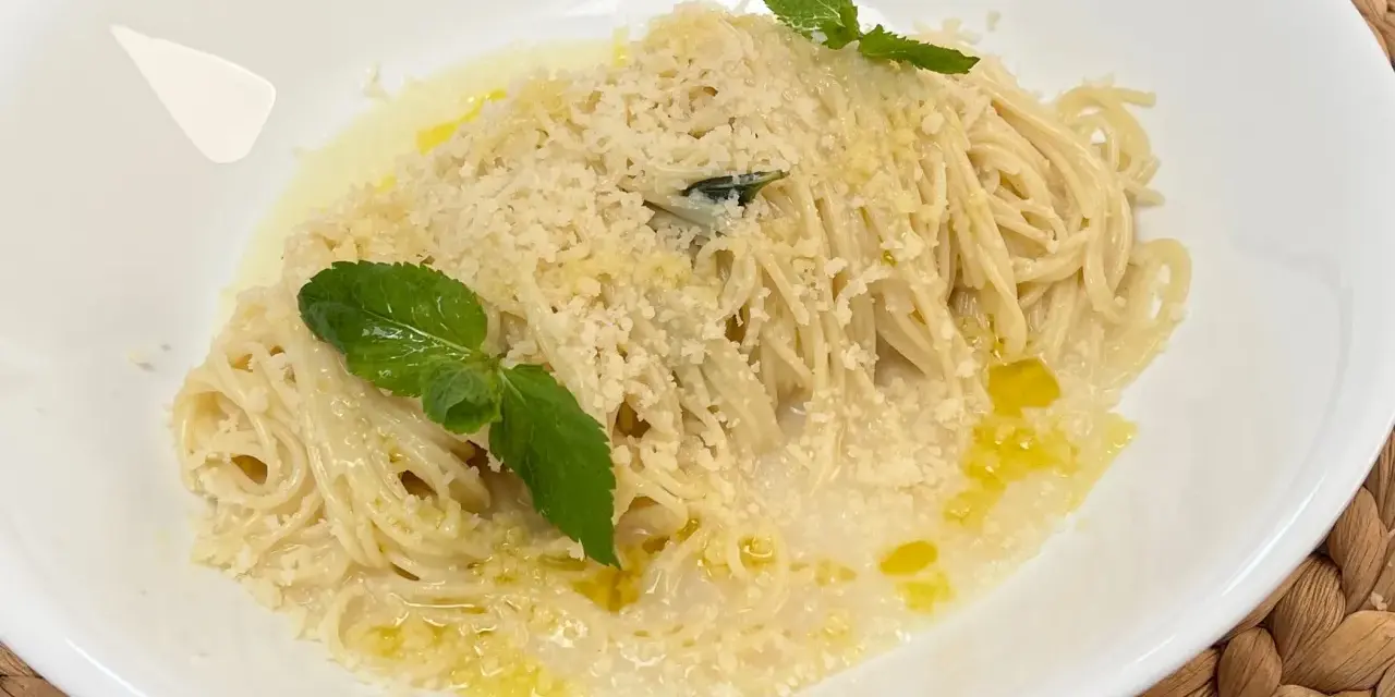 Spaghetti al limone cremosi, cosparsi di parmigiano e guarniti con foglie di menta fresca. Un piatto profumato e invitante.