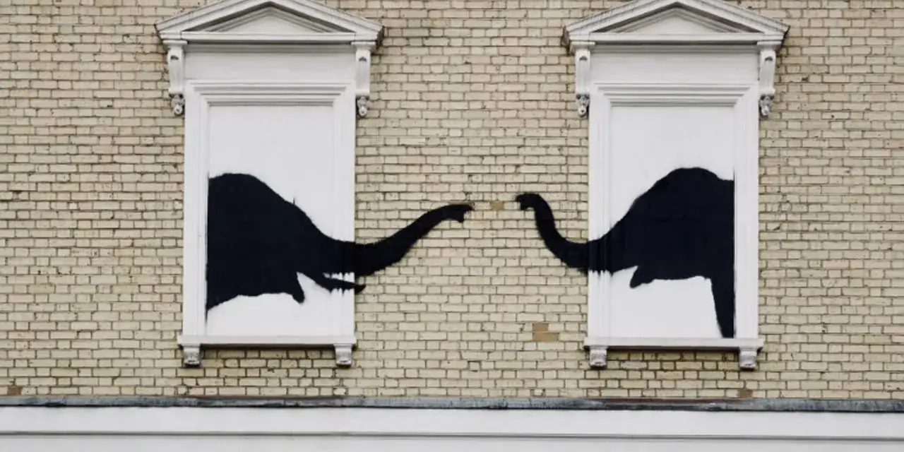 Œuvre Banksy : deux éléphants noirs se touchent la trompe à travers deux fenêtres sur un mur de briques.