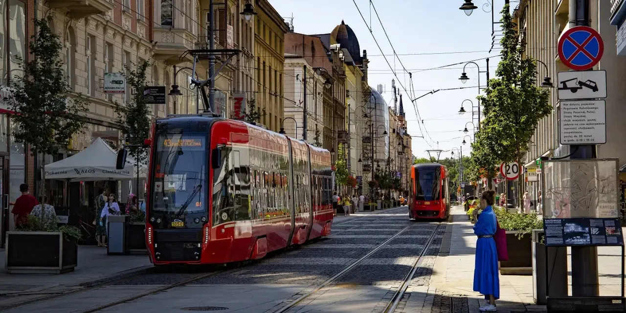 Czerwony tramwaj na ulicy w Katowicach. W tle kamienice i inny tramwaj. To widok na katowice stare miasto.