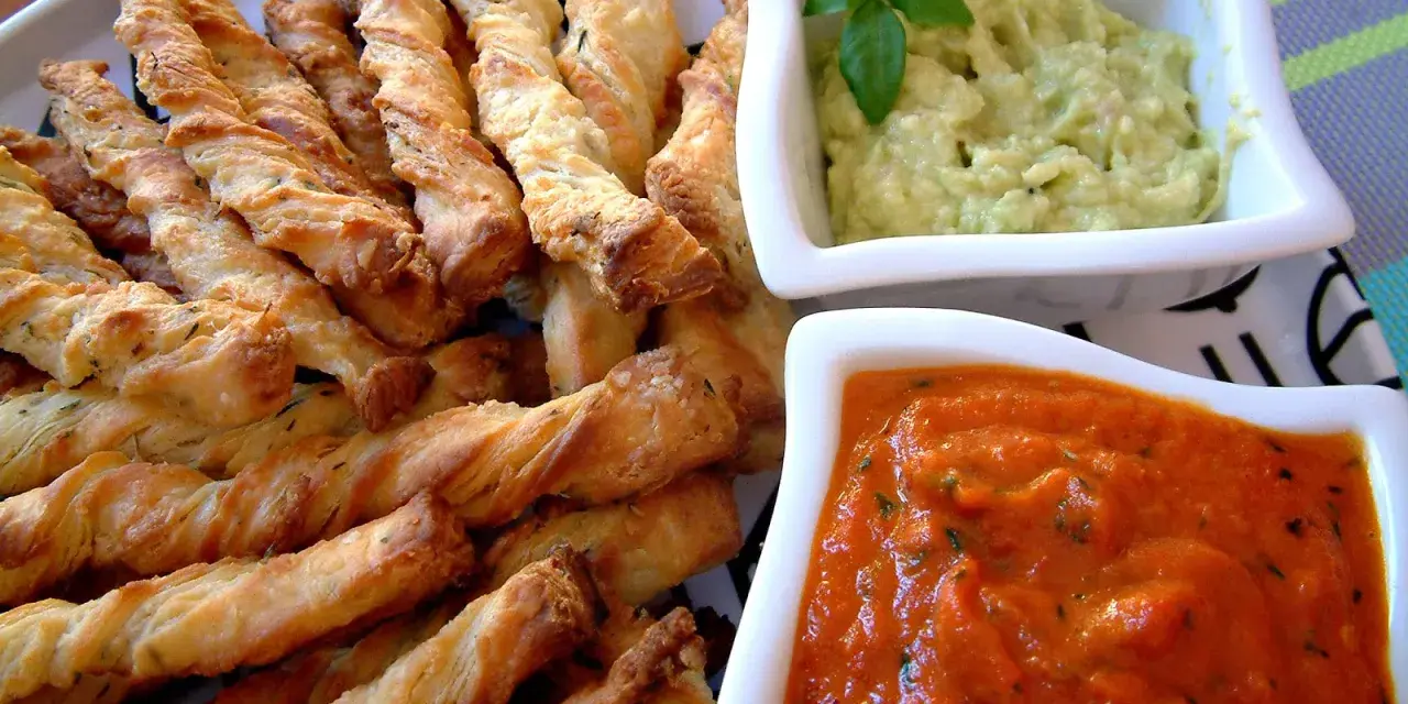 Chrupiące paluszki grissini z ziołami, idealne do podania z kremowym guacamole i pikantnym sosem pomidorowym.