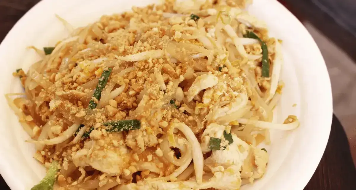 Pyszny pad thai oryginalny przepis z kurczakiem, kiełkami i orzeszkami ziemnymi na białym talerzu.
