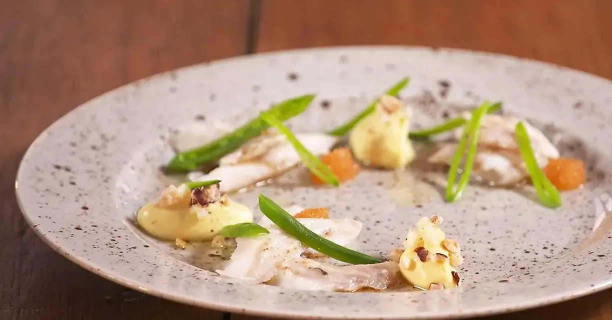 Vacker tallrik med piggvar recept: vit fisk, gröna bönor, orange rom och en krämig sås med nötter.