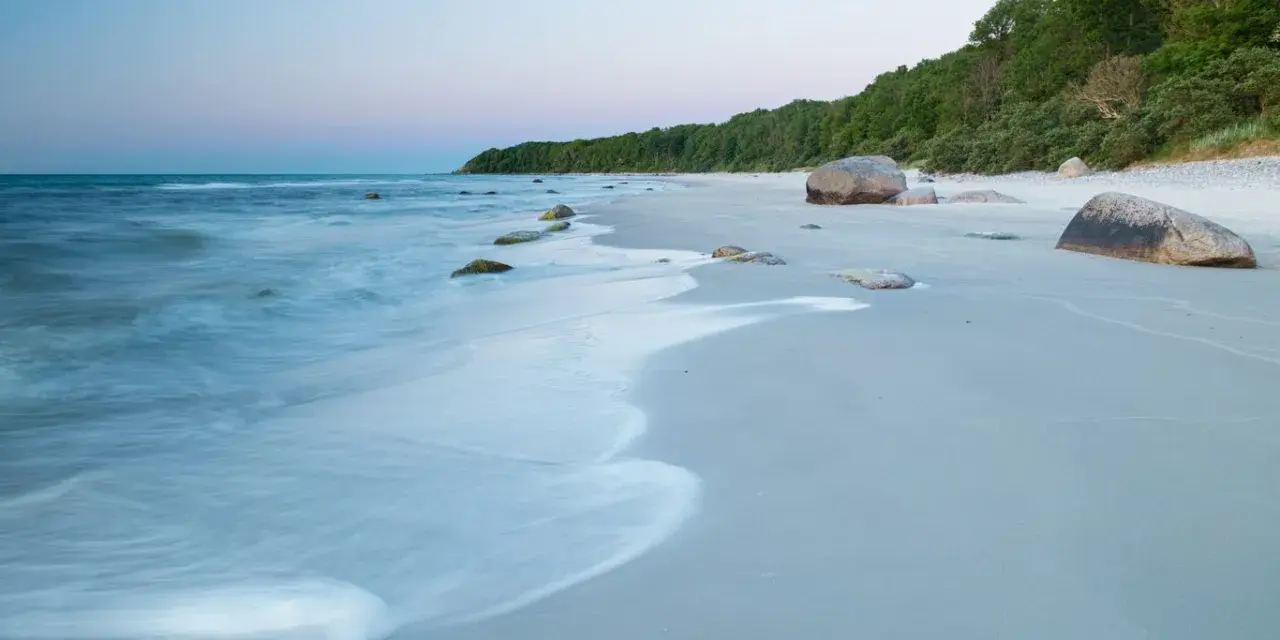 Spokojne plaże nad Bałtykiem o świcie, z delikatnymi falami i kamieniami na piasku.