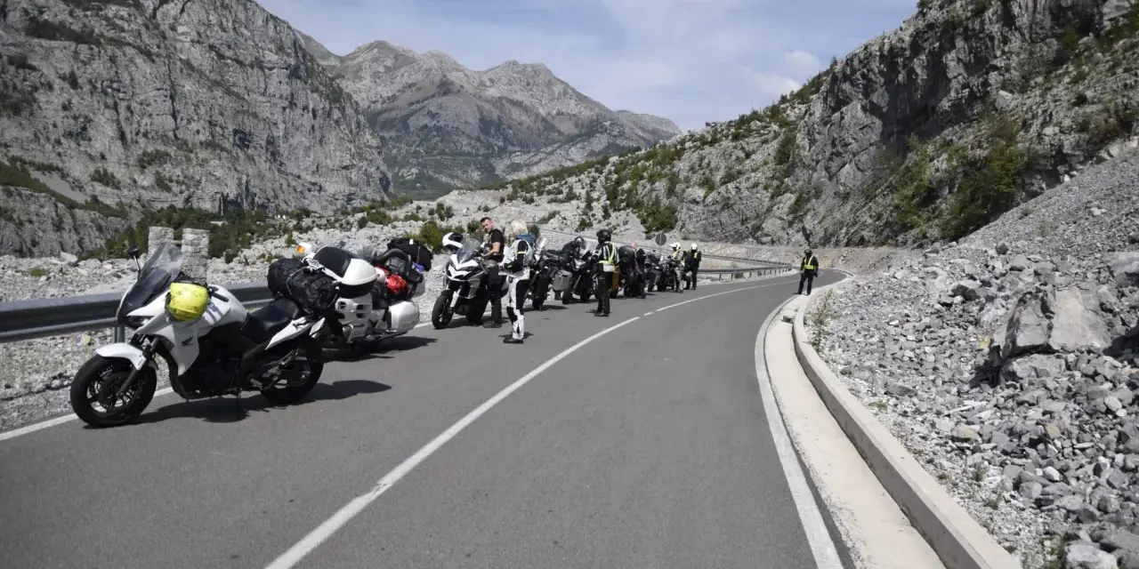 Grupa motocyklistów zatrzymała się na malowniczej drodze w Albanii, podziwiając spektakularne widoki gór.