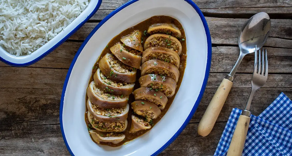 Calamares rellenos en salsa, servidos en una bandeja ovalada junto a un bol de arroz blanco. Cubiertos con cebollino picado.
