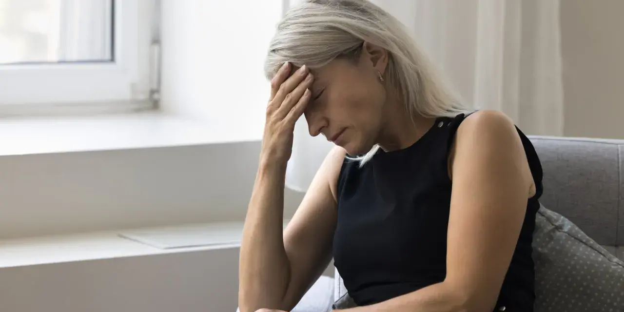 Kobieta z ręką na czole, cierpiąca na zawroty głowy związane z menopauzą.