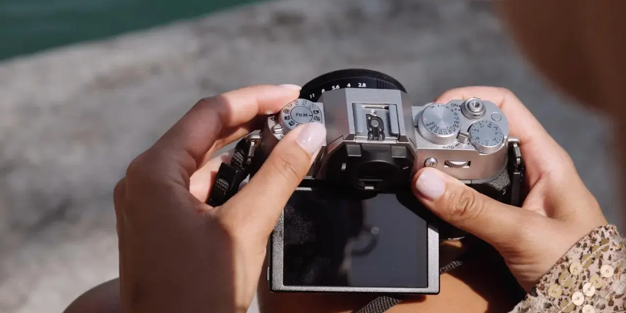 Dłonie trzymają srebrny aparat Fujifilm XT50, obracając pokrętło trybów filmowych.