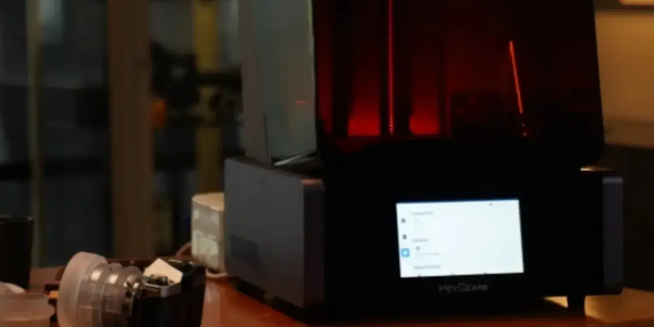 A HeyGears resin printer with a red interior light. Beside it, a camera lens. This setup hints at the process of how long to cure resin prints.