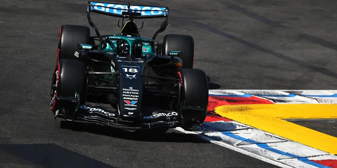El coche de F1 Aston Martin número 18 se inclina en una curva, con sus neumáticos rozando la línea de la pista.