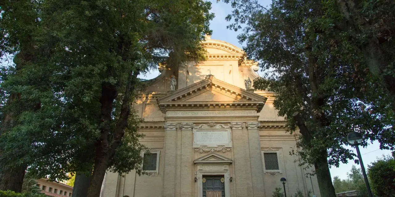 A serene church facade at Tre Fontane, Rome, bathed in golden light, framed by lush green trees.
