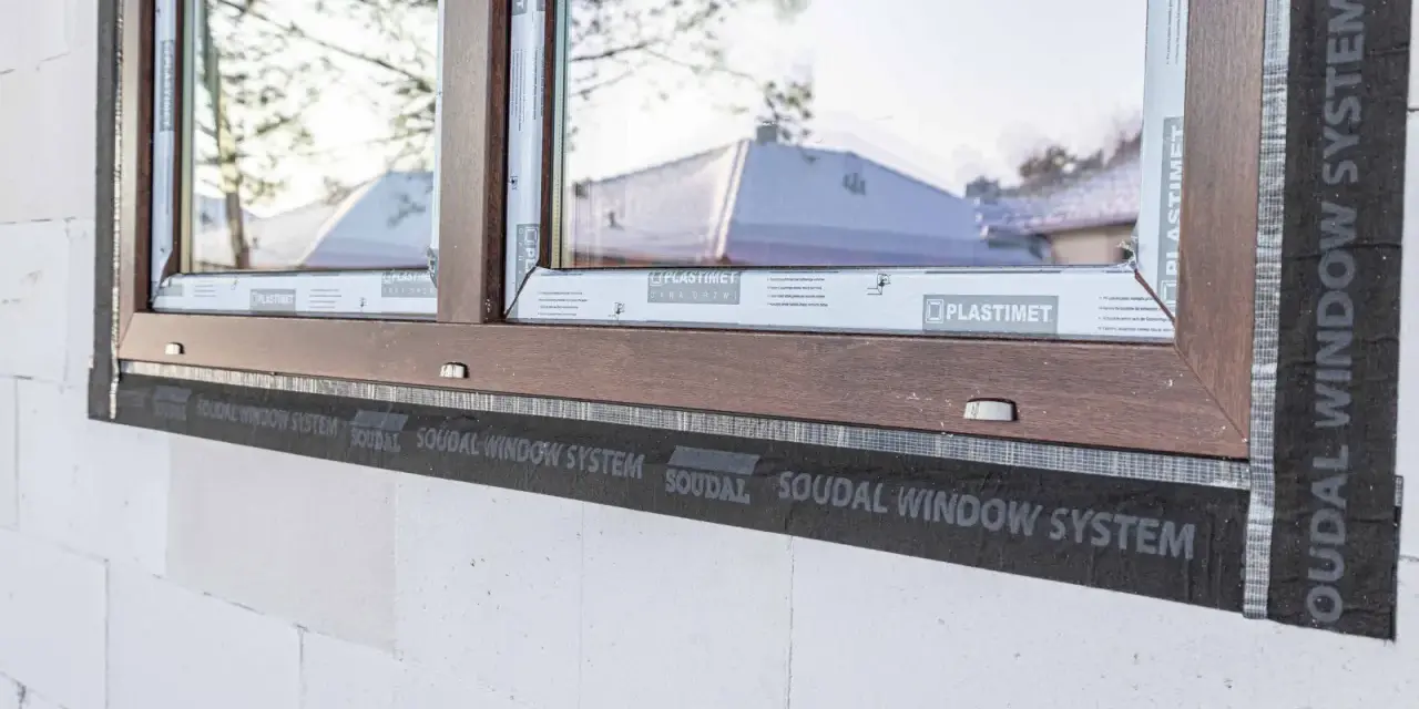 Ciepły montaż okien z użyciem taśmy Soudal Window System. Brązowa rama okienna na tle białego pustaka.