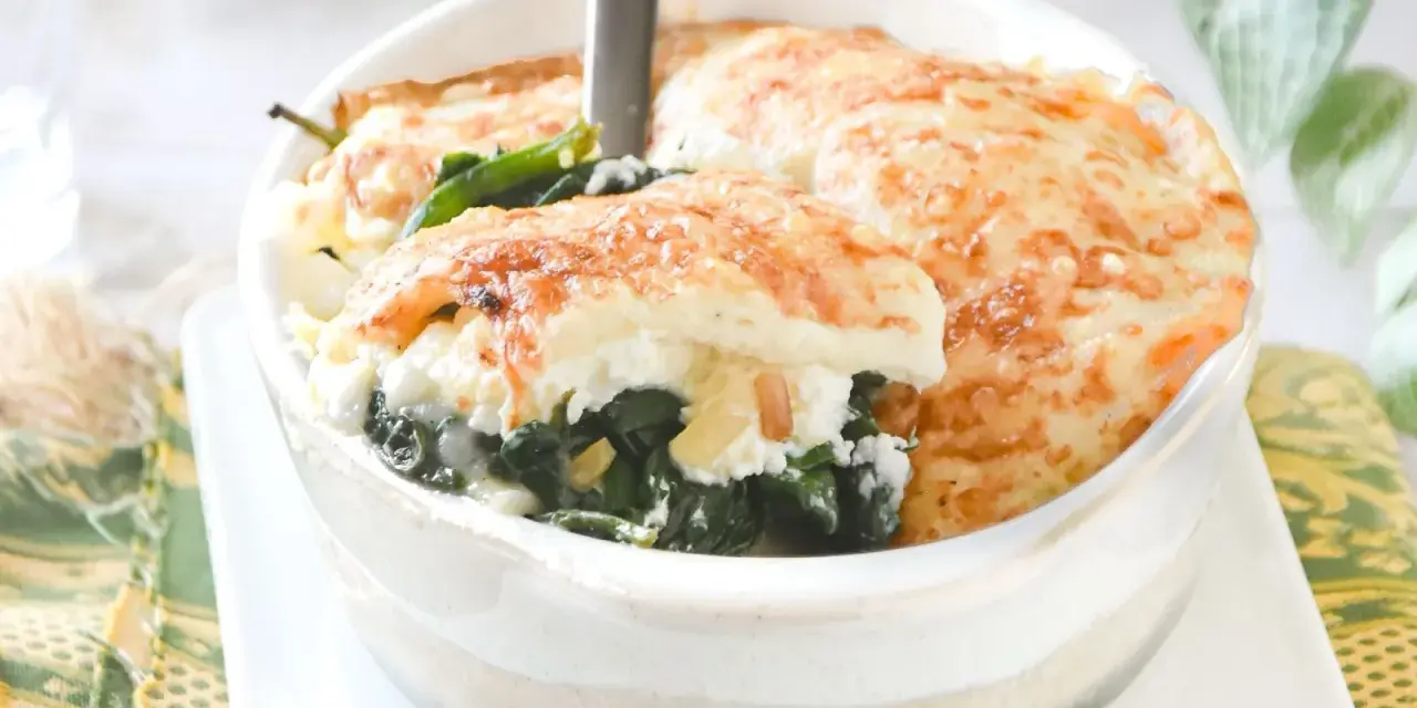 Deliciosa lasaña de espinacas gratinada, servida en un cuenco blanco. El queso dorado y burbujeante cubre las capas de espinacas y ricotta.