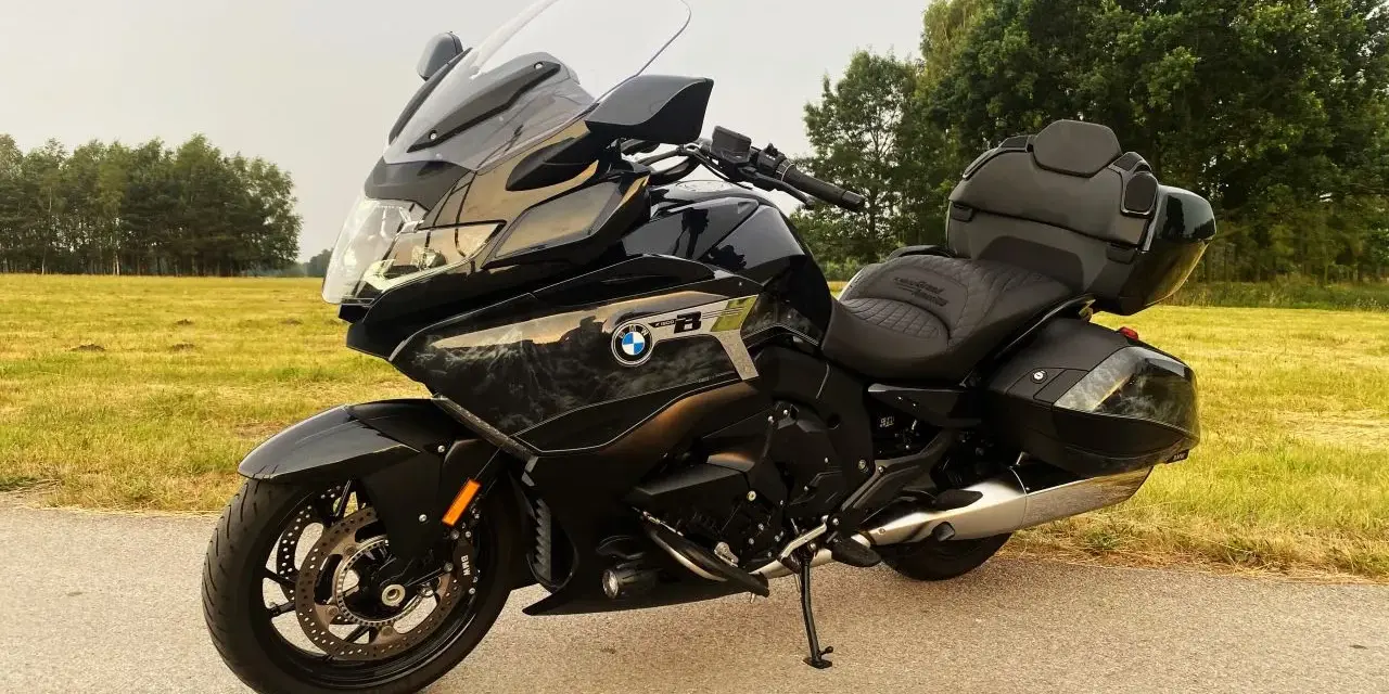 Czarny motocykl BMW K1600 Grand America z kuframi, gotowy na daleką podróż pośród zielonych pól i drzew.