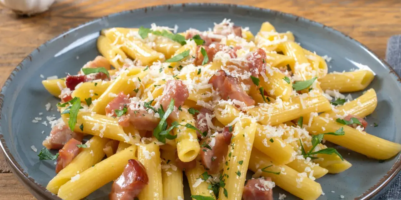 Penne z boczkiem i parmezanem, posypane natką pietruszki. Pyszny makaron z serem i boczkiem na talerzu.