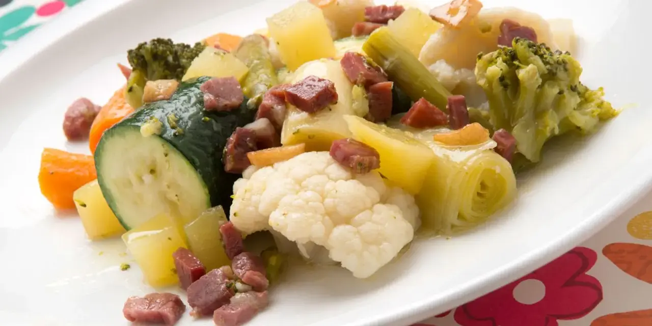 Un colorido panache de verduras con brócoli, coliflor, calabacín, zanahoria y patatas, salpicado de trocitos de jamón.